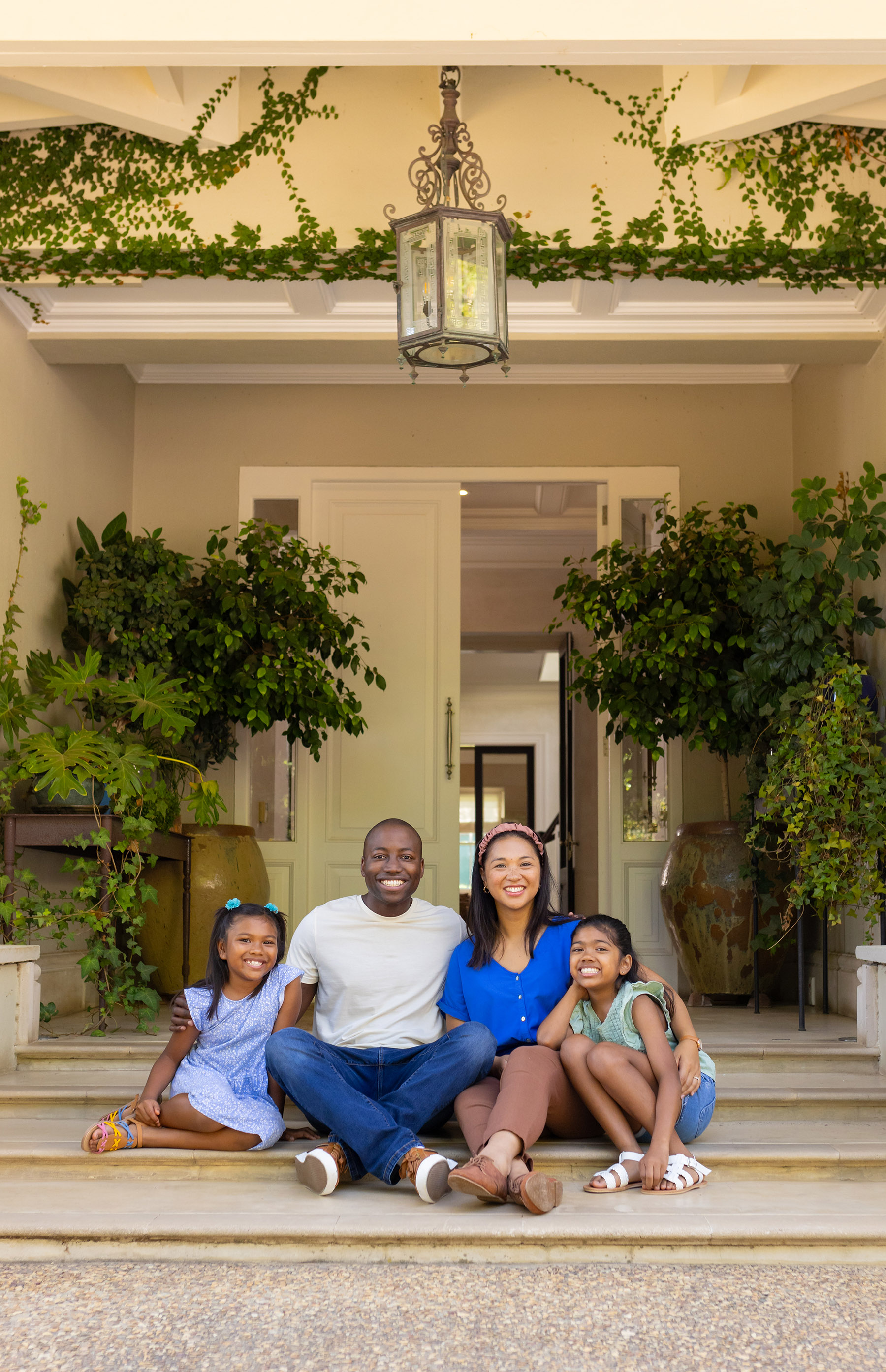 Happy family of four with daughters sitting on front steps of their home, smiling together. togetherness, outdoors, happiness, multiracial parents, daughters, bonding